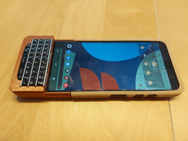 An image of a smarphone sitting on a lightly-colored wooden table. It has a tan case surrounding it on the top 2/3, and a copper case holding a BlackBerry Q10 keyboard jutting out over the bottom of the phone.