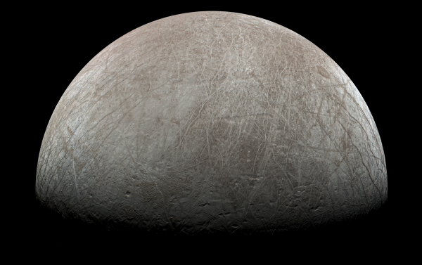 An image of the surface of Europa. The top half of the sphere is illuminated with the bottom half dark. The surface is traced with lineae, long lines across its surface of various hues of grey, white, and brown. The surface is a brown-grey, somewhat like Earth's Moon with the highest brightness areas appearing white.