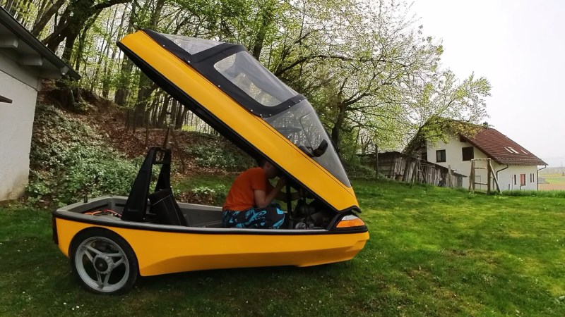 A yellow, three wheeled vehicle with a canopy that opens upward over the body. It looks a little like the cockpit of a jet figher.