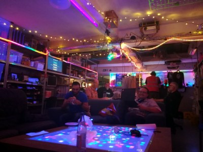 A hackerspace room lit by festoons of multi coloured LED strips.
