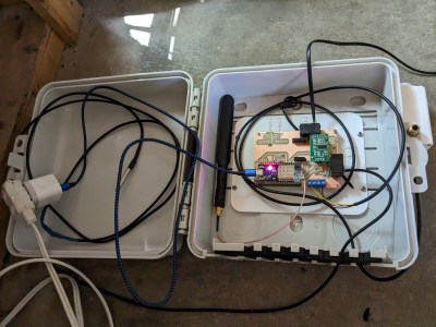 A white outdoor-rated box opened to reveal electronics to monitor a beehive.