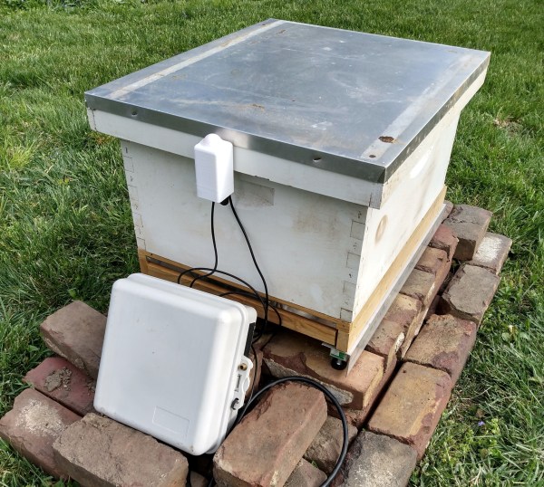 A beehive sits on bricks with an outdoor-rated box full of electronics to monitor the hive.