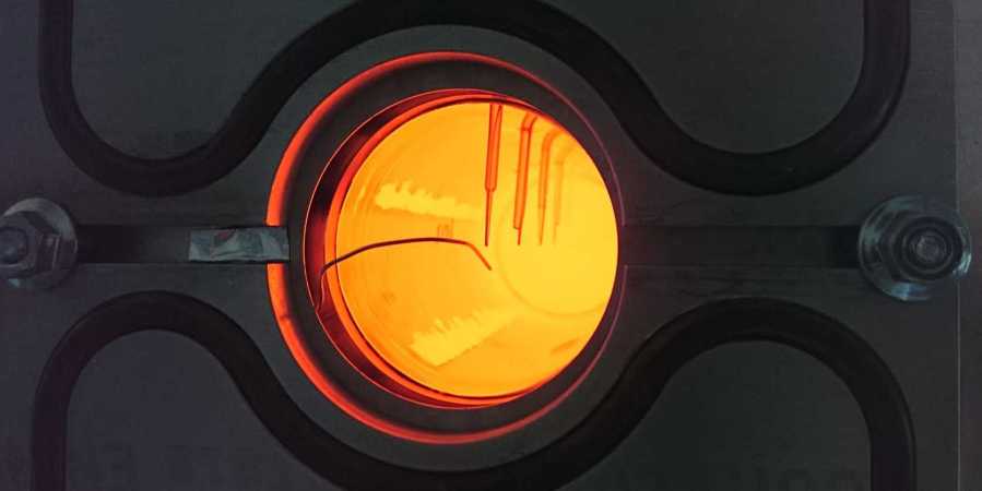 An image of an orange, translucent glowing quartz rod. Thermocouples can be seen at intervals along the rod looking in.