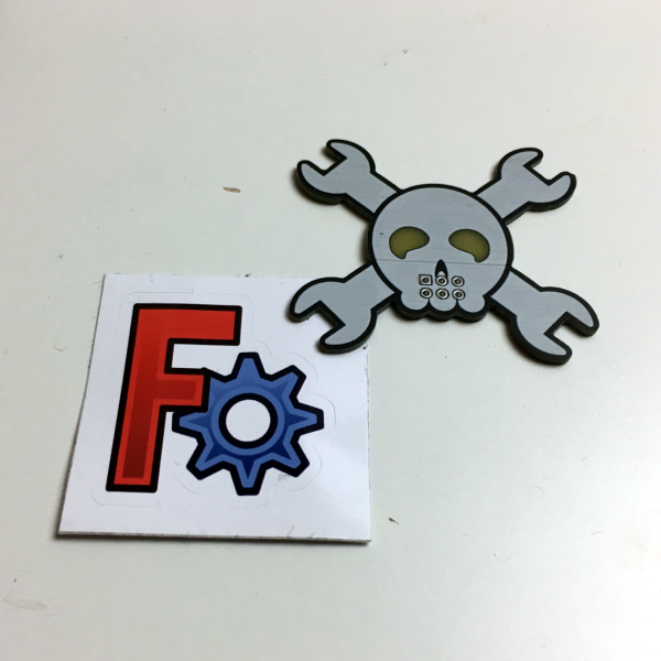 A Hackaday Jolly Wrencher SAO PCB and a FreeCAD sticker next to each other