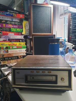 A small 8-track player and equally small speakers, plus a stack of VHS tapes. 