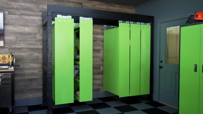 Bright green shelving units suspended with silver hardware from a black frame. They are against a dark wooden wall.