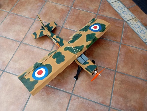 A painted RC plane made of cardboard. It has an orange propeller and camo-esque markings along with concentric blue, white, and red circles near the wingtips.