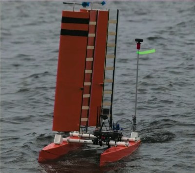 An orange catamaran with two orange sails sticking up out of the starboard hull. A number of antennae and instruments jut out from the deck.