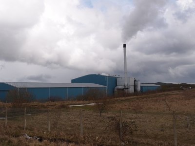 A nondescript industrial building with a slender chimney, against a grey cloudy sky.