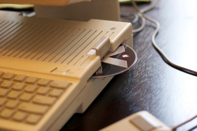 A Mac OSX install DVD peeks out from the disc slot on a beige Apple IIc. You'd never guess this was originally a floppy drive.