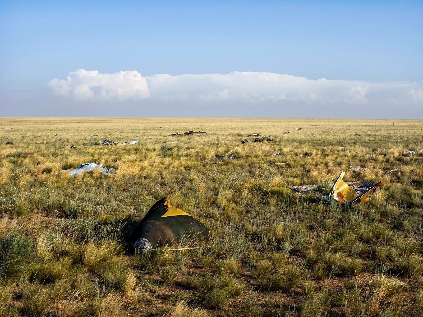 A wide angle photo of a Kazakhstan grassy steppe littered with rusty abandoned pieces of Soyuz space capsules