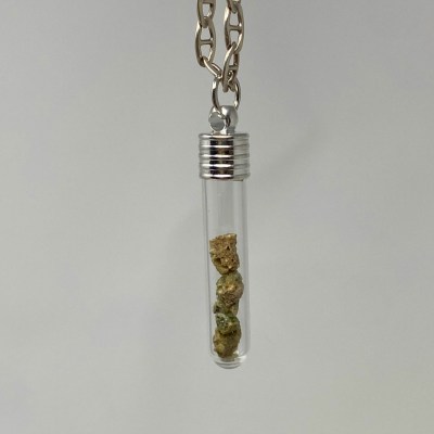 A see-through vial pendant with several small samples of Trinitite.