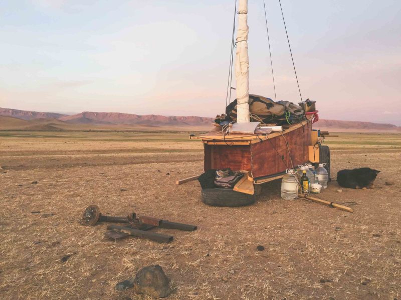 A vaguely boat-shaped vehicle with three wheels and a mast. It sits in a barren-looking plain with short mountains in the distance