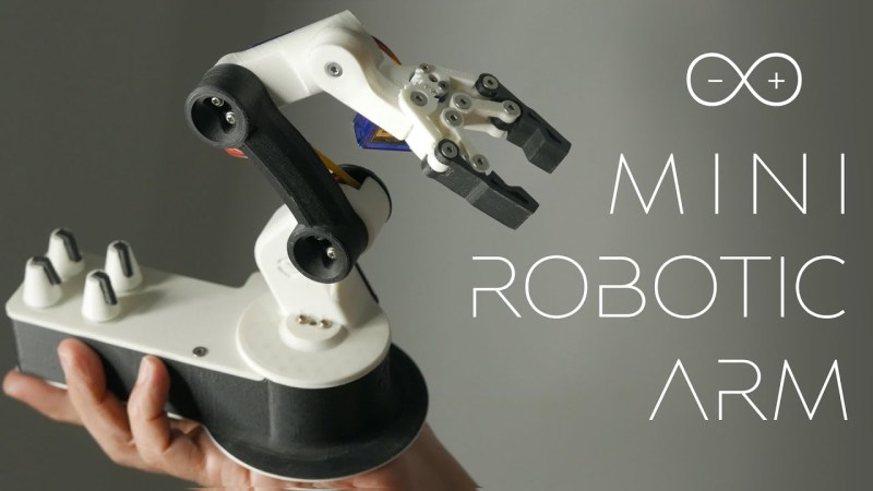 A black and white robot arm is held in a human hand against a grey background. Next to it, in white lettering, is the Arduino logo and the text, "Mini Robotic Arm."