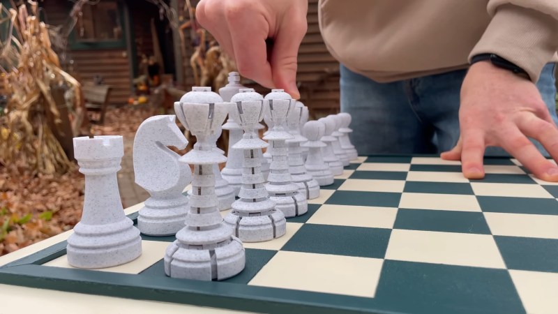 White pieces on a teal and white chess board. The line of pawns shows three segmented queens in the foreground, one piece being pressed by a man's hand from above in a state between queen and pawn, and the remainder of the pawns in the background in the pawn state.