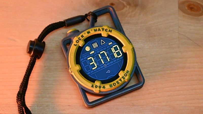 An image of a black carabiner-esque frame surrounding a round, yellow bezeled digital watch. A black paracord lanyard is attached to the top right of the black frame and a yellow button is visible near the top left of the frame.