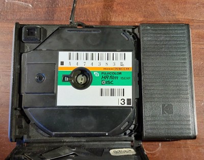 The back of a disc camera with the flap open, and a film cartridge inside.