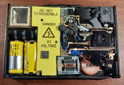 The inside of a Disc camera. On the left is the flash tube and the battery, in the middle the electronics behind a protective yellow warning cover, on the right the film advance and shutter mechanism.