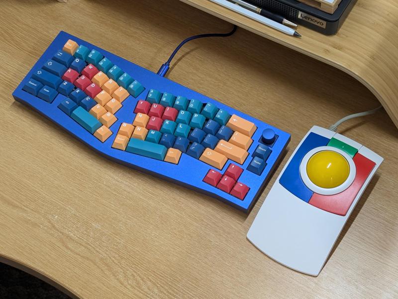 A lovely '90s kid setup with primary-colored GMK Panels keycaps on a blue Alice layout, plus a primary-colored trackball.