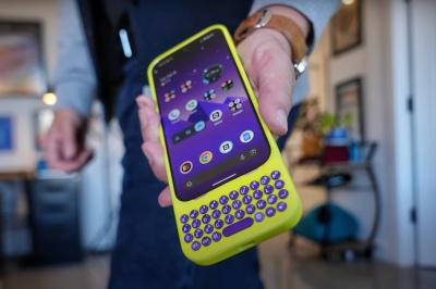 A person holds out an Android phone with a Clicks keyboard case in neon yellow with purple keys.