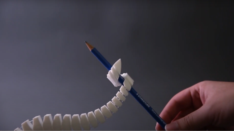 A human hand is shown in the bottom right corner of the picture, holding one end of a pencil. A white, segmented, mechanical tentacle extends from the bottom left corner of the image and wraps around the other end of the pencil.