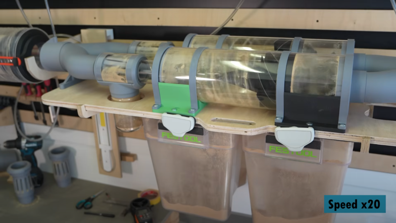 Two clear acrylic tubes are shown in the foreground. Swirls of sawdust are visible on the inside of the tubes, and the tubes are held in place by grey plastic connectors. Below the tubes, there are two clear plastic tubs containing sawdust.
