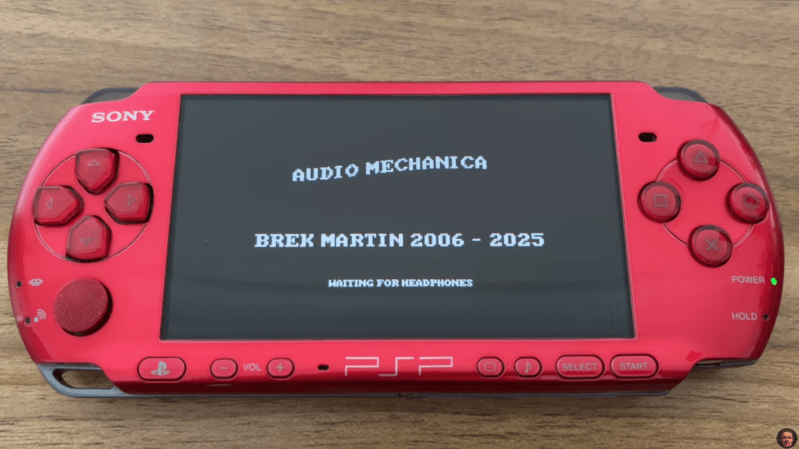 A red Sony PSP gaming console is shown, displaying the lines “Audio Mechanica,” “Brek Martin 2006-2025,” and “Waiting for Headphones.”