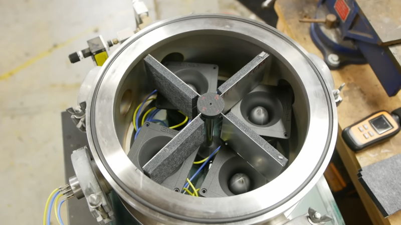 A circular metal vessel is shown, with a symmetrical rotor of four vanes standing inside. At the bottom of the vessel are four loudspeakers.