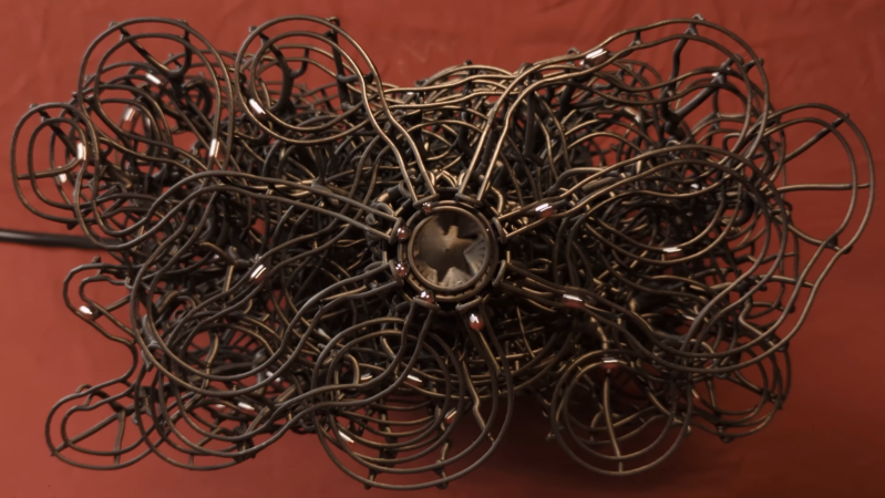A central circular element is releasing steel ball bearings into a complex nest of eight intertwined plastic paths.