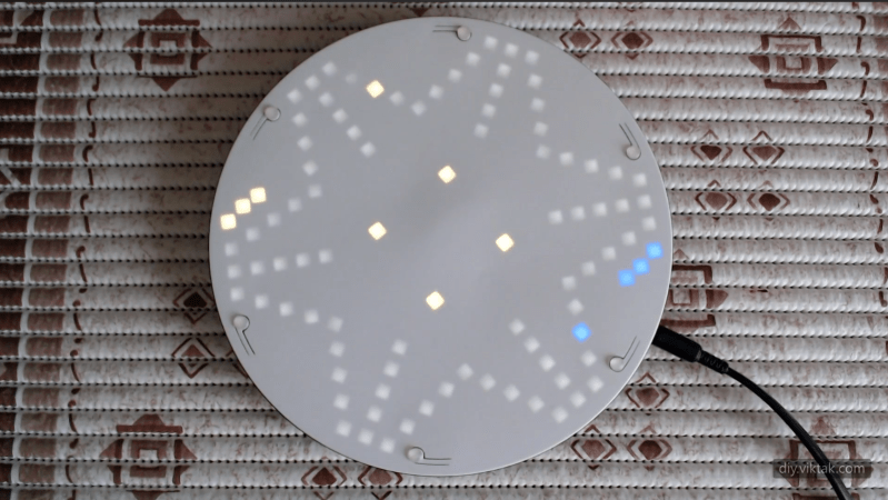 A circular 3D-printed board is shown, with a roughly star-shaped pattern of white LEDs glowing through the surface. Yellow and green LEDs are also visible through the surface at a few points.