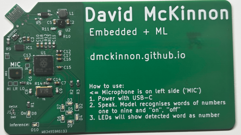 A circuit board in the shape of a business card is shown. The circuitry is confined to the left side of the board, and the rest is used for text.