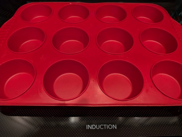A red silicone cupcake pan sits on a black glass inductive stove cooktop. The word induction is written in white text on the glass of the stove.