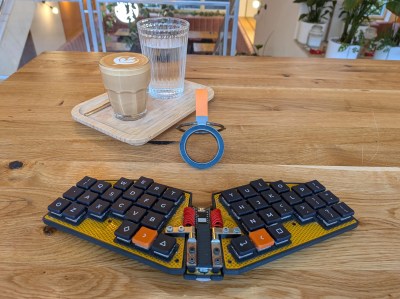 A small, folding split sits on a wood table with a hot latte in a glass and a glass of water on a tray.