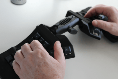 Two hands rest on a joined split keyboard with keywells and tenting. The two halves are on ball joints and connect in the middle.