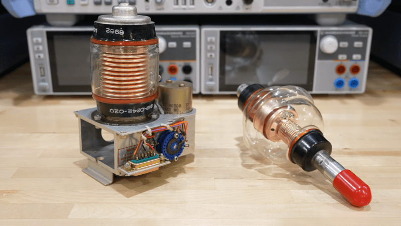 A pair of glass vacuum tubes can be seen on a workbench, each with complex copper structures inside. One is mounted on top of a metal chassis with a motor and some other circuitry visible.