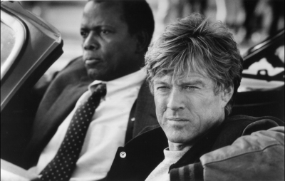 Robert Redford and Sidney Poitier in an open-topped convertible. Black and white.