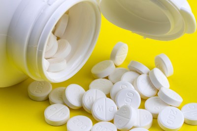 Round, white pills spill from a bottle against a yellow background.
