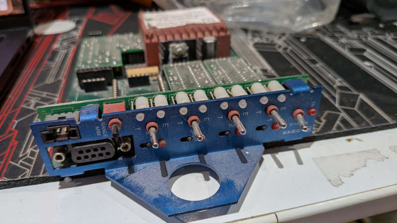 A circuit board card is shown, with a blue panel on one side. On the panel are switches and an RS-232 port.