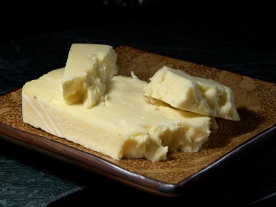 A slice of cheese on a cheese board, with a piece crumbled off.