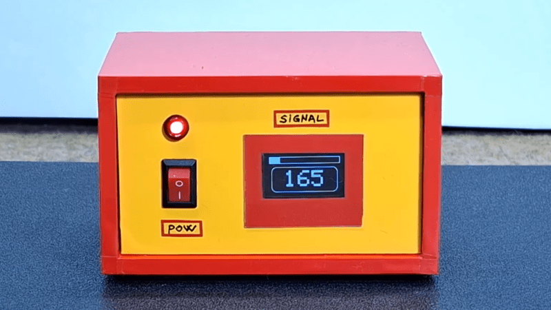 A red box with a yellow front panel is shown. The front panel contains a power switch, an indicator light, and a small OLED display.