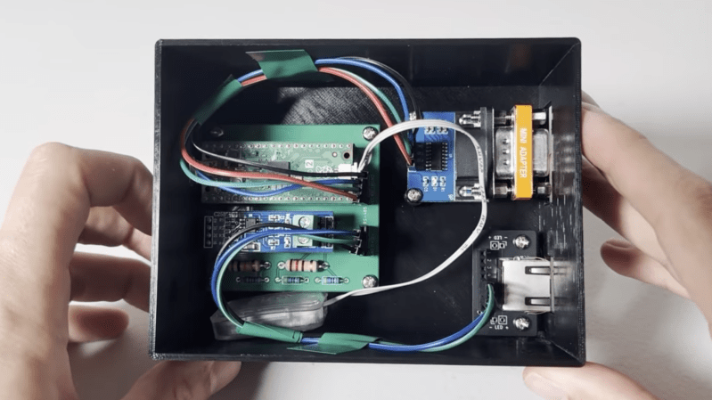 A black plastic box is shown, with a green circuit board inside. The circuit board is wired to an RS-232 connector and an RJ-45 connector.