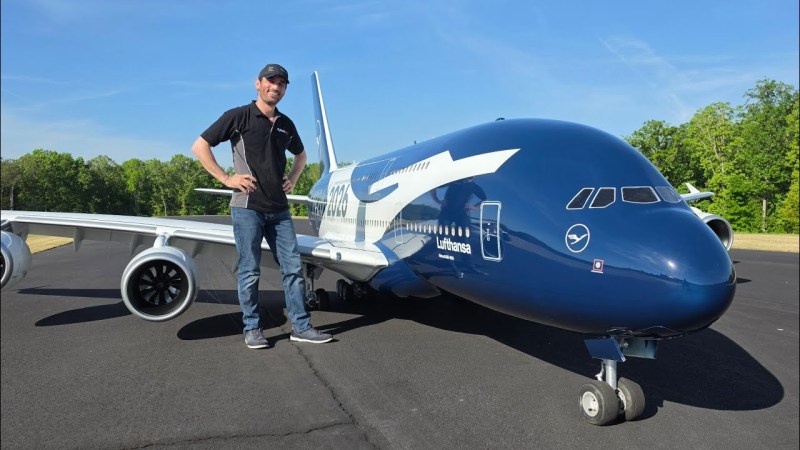 A man standing next to an RC model of an Airbus A380 aircraft. The fuselage is at elbow height and the tailfin appears to be over his head.