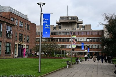 A brick-and-concrete university building, a lawn and paved path in the foreground.