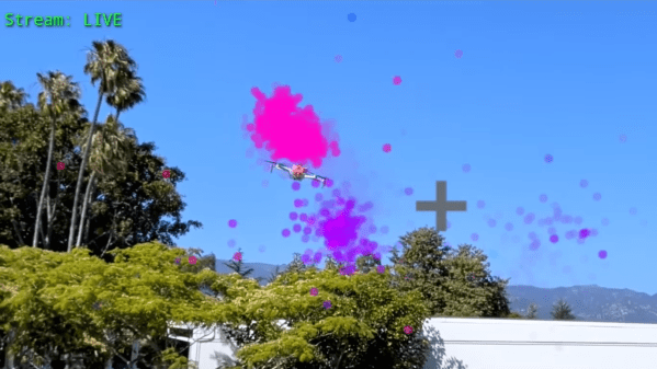 A drone is shown flying above some trees and a building. A pink cloud of dots appears above the drone, and a purple cloud below the drone. Grey crosshairs are to the right of the drone.