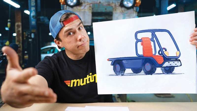 A man in a black shirt with the word "Mutiny" in yellow letters next to a short set of red, orange, and yellow stripes like a 1970s truck graphics package guestures to the camera while holding a sketch of a blurple truck consisting of a tube frame cab, flat loading deck, orange seat, and a silvery front bumper.