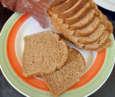 A loaf od sliced brown bread, cascading from its bag onto a plate.