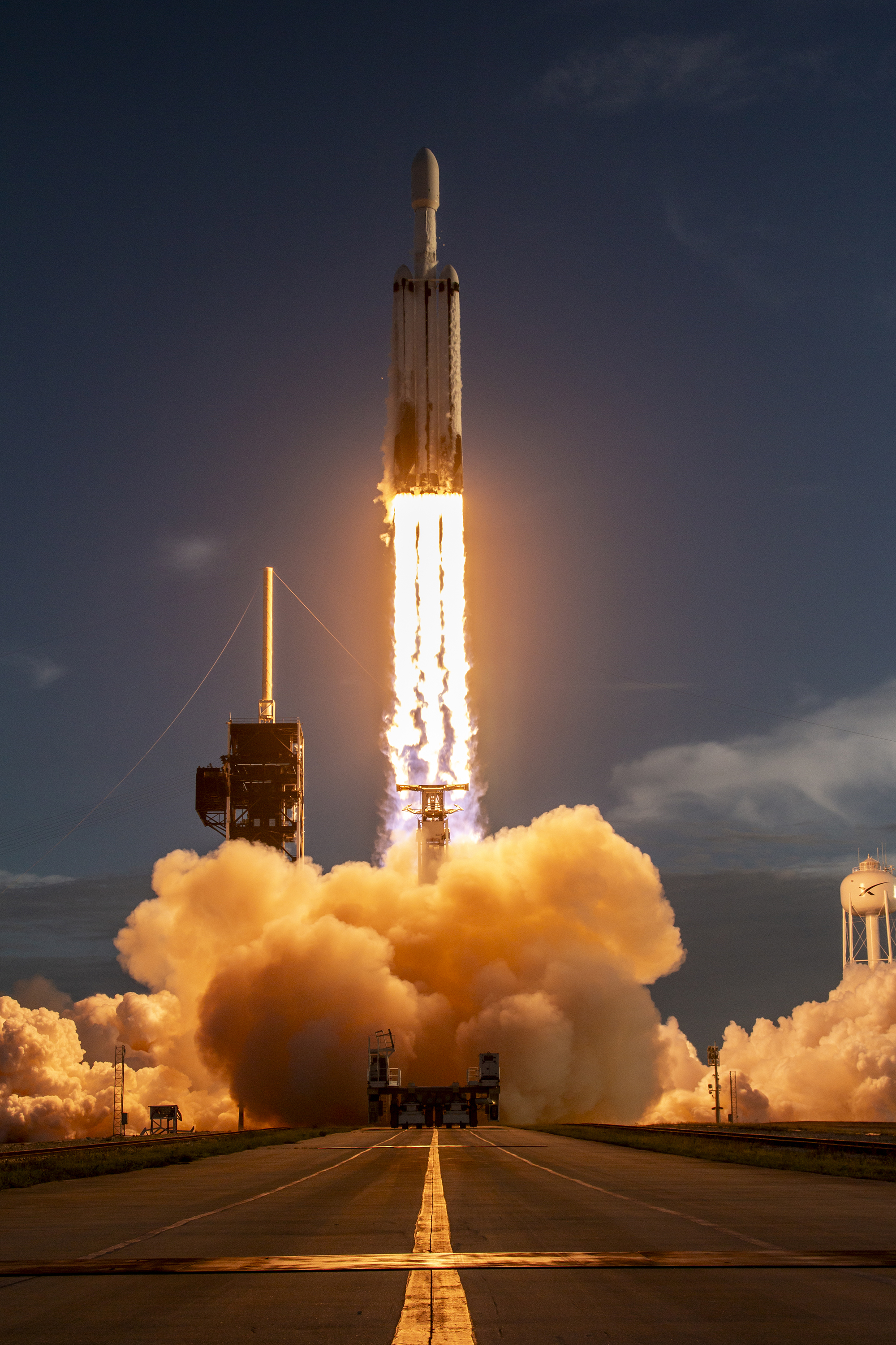 A rocket lifts off from a coastal launch pad, sending bright flames and a plume of white smoke across the ground.