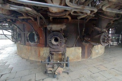 The side of a furnace, lots of pipework, in front of us is a hole in the rusty steel side where the air would have been injected.