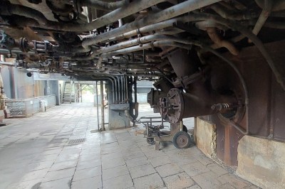 A maze of pipes extends along the top of the image, daylight in visible on the left, and on the right is the concrete edge of the furnace. and
