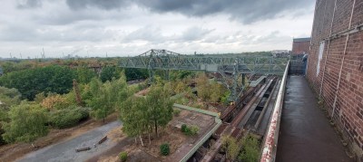 A view out over a wooded post industrial landscape against a grey cloudy sky. In the foreground is a hiuge traverser crane.